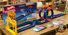 An open display of the Hot Wheels Wild Drive Drag Race set with track loops and two racing cars on a wooden table available at Juniors Toys